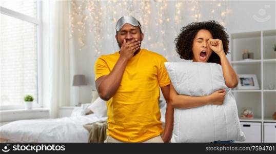 morning, bedtime and people concept - african american couple with eye sleeping mask and pillow yawning over bedroom background. sleepy african american couple over bedroom