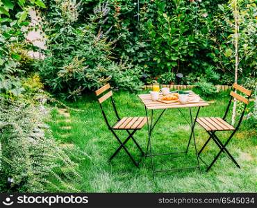 Morning Breakfast In Green Garden With French Croissant, Coffee Cup, Orange Juice, Tablet and Notes Book On Wooden Table