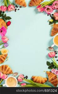 Morning coffee, croissants and a beautiful flowers on blue background. Cozy breakfast frame. Flat lay composition for bloggers, magazines, web designers, social media and artists.