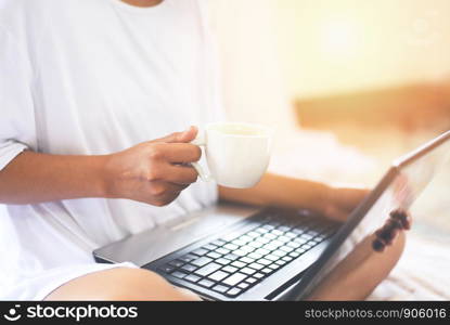 Morning coffee cup / woman holding coffee cup by hand with laptop on the bed