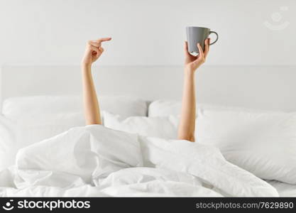 morning, comfort and people concept - young woman with cup of coffee lying in bed at home bedroom. woman with cup of coffee lying in bed