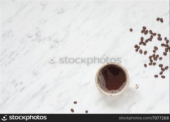 Morning composition with a cup of black coffee and coffee beans on a marble surface with space for text, top view