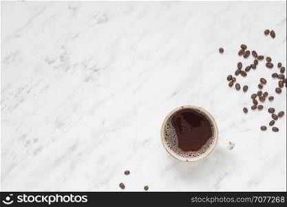 Morning composition with a cup of black coffee and coffee beans on a marble surface with space for text, top view