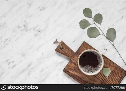 Morning composition with a cup of black coffee and eucalyptus green branch on a marble surface with space for text, top view