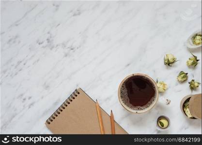 Morning composition with a cup of black coffee, chocolate candies and a notebook on a marble surface with space for text, top view
