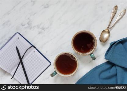Morning composition with two cups of black coffee and a notebook on a marble surface, with space for text, top view