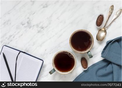 Morning composition with two cups of black coffee, blue napkin and notebook on a marble surface, with space for text, top view