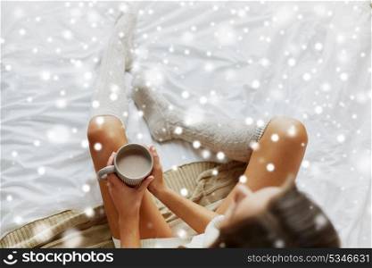 morning, coziness, winter and people concept - close up of young woman with cup of coffee or cacao in bed over snow. close up of woman with cocoa cup in bed at home