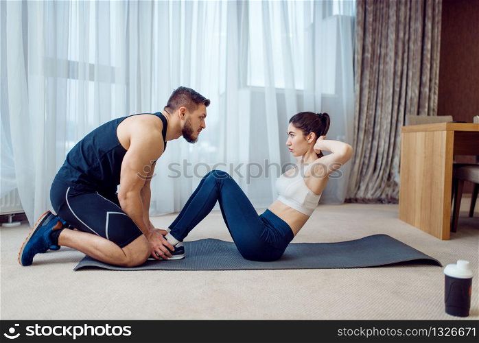 Morning fit training of couple at home. Active man and woman in sportswear doing exercise on the press in their house, healthy lifestyle, physical culture. Morning fit training of couple at home
