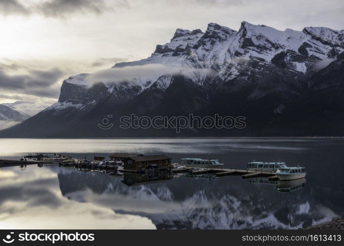 Morning fog burns off of a mirror still Lake Minnewanka in Banff on an early June morning.