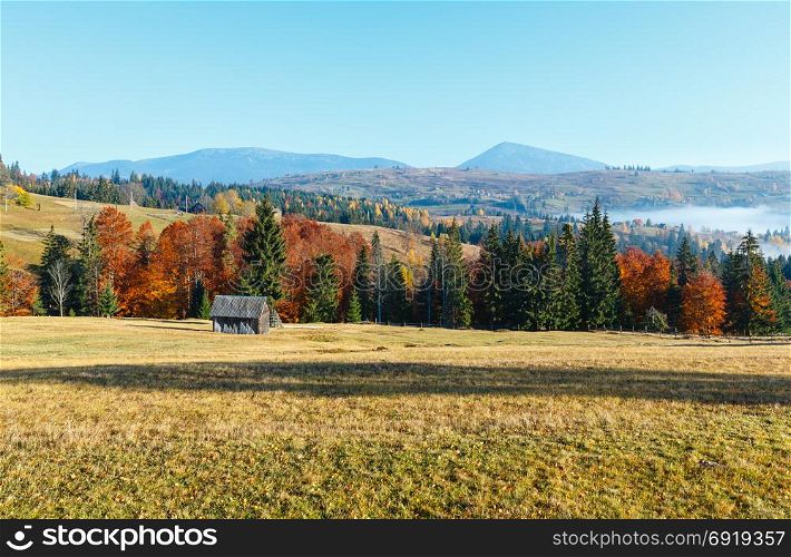 Morning fog, colorful trees and wooden shed on the slopes of the Carpathian Mountains (Yablunytsia village, Ivano-Frankivsk oblast, Ukraine). Autumn rural landscape.