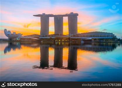 Morning in Singapore. Three buildings of the hotel in the form of a ship are reflected in the calm water of Marina Bay. The rising sun painted the sky in orange and red. Orange Dawn at Marina Bay