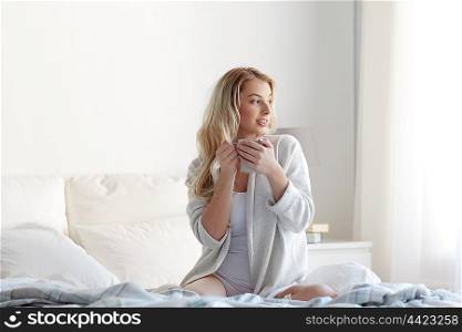 morning, leisure and people concept - happy young woman with cup of coffee or tea in bed at home bedroom