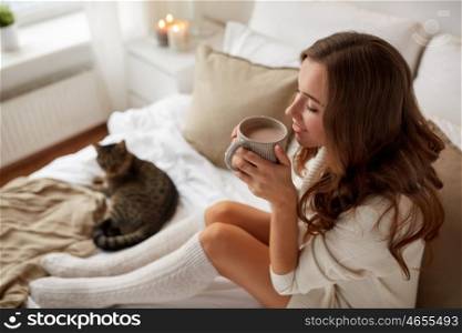 morning, leisure, christmas, winter and people concept - happy young woman with cup of coffee or tea in bed at home bedroom