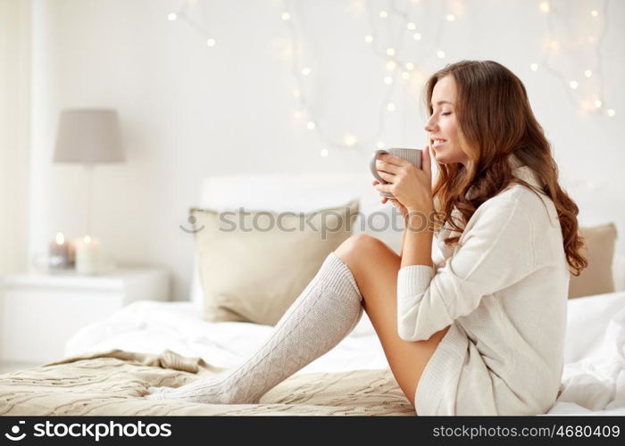 morning, leisure, christmas, winter and people concept - happy young woman with cup of coffee or tea in bed at home bedroom