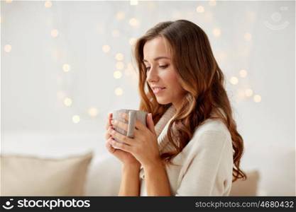 morning, leisure, christmas, winter and people concept - happy young woman with cup of coffee or tea at home