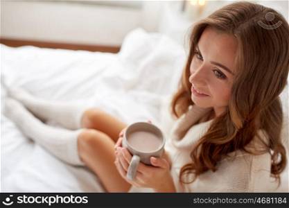 morning, leisure, christmas, winter and people concept - happy young woman with cup of coffee or cocoa in bed at home