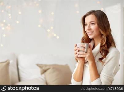 morning, leisure, christmas, winter and people concept - happy young woman with cup of coffee or tea at home
