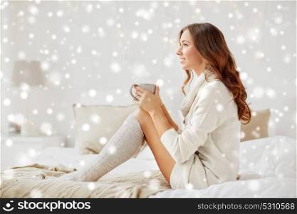 morning, leisure, christmas, winter and people concept - happy young woman with cup of coffee or tea in bed at home bedroom over snow. happy woman with cup of coffee in bed at home