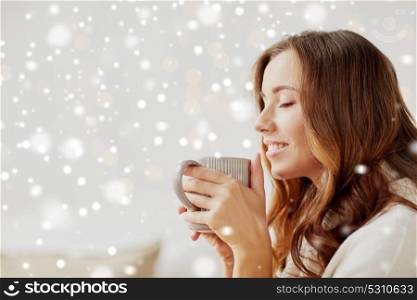 morning, leisure, christmas, winter and people concept - happy young woman with cup of coffee or tea at home over snow. happy woman with cup of tea or coffee at home