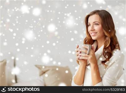 morning, leisure, christmas, winter and people concept - happy young woman with cup of coffee or tea at home over snow. happy woman with cup of coffee or tea at home