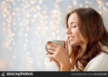 morning, leisure, christmas, winter and people concept - happy young woman with cup of coffee or tea at home. happy woman with cup of tea or coffee at home