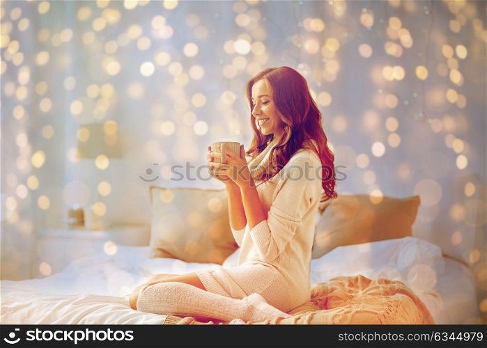 morning, leisure, christmas, winter and people concept - happy young woman with cup of coffee or tea in bed at home bedroom. happy woman with cup of coffee in bed at home