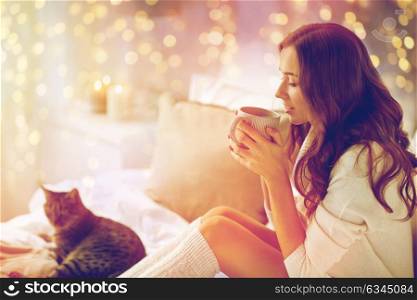 morning, leisure, christmas, winter and people concept - happy young woman with cup of coffee or tea in bed at home bedroom. happy woman with cup of coffee in bed at home