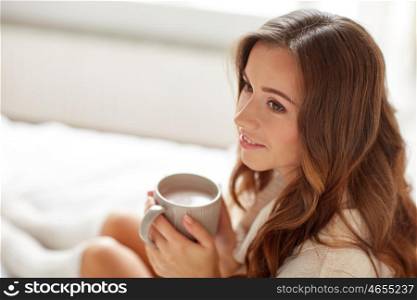 morning, leisure, winter and people concept - happy young woman with cup of coffee or cocoa in bed at home