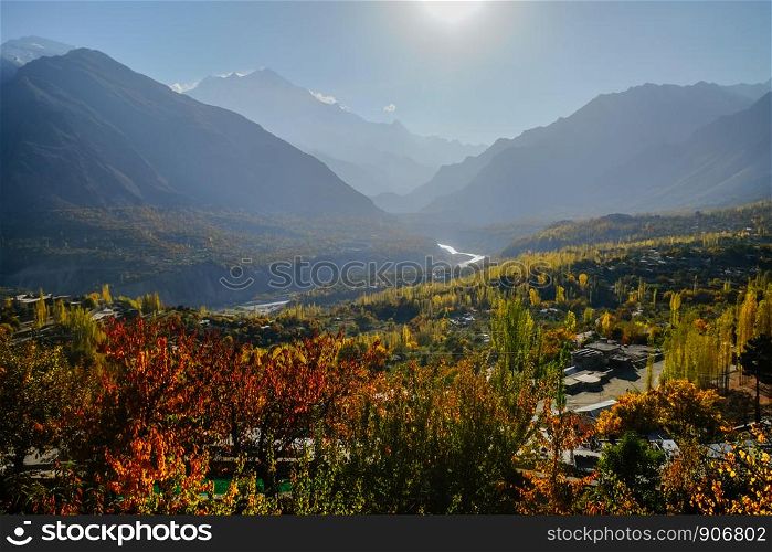 Morning natural sunlight lit colorful foliage trees in forest and mountains in Karakoram range in the background. Hunza Nagar valley in autumn season. Gilgit Baltistan, Pakistan.