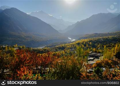 Morning natural sunlight lit colorful foliage trees in forest and mountains in Karakoram range in the background. Hunza Nagar valley in autumn season. Gilgit Baltistan, Pakistan.