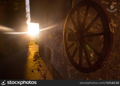 morning on a farm in the village. small street and dawn rays. wooden wheel from the cart in the foreground