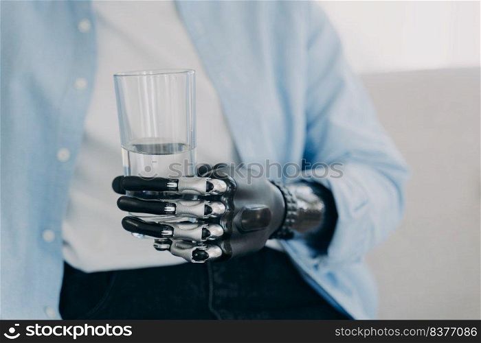 Morning routines of disabled person. Girl is using futuristic robotic arm prosthesis and holding glass of water at home. Modern bionic prosthesis. Healthy lifestyle after&utation surgery.. Morning routines of disabled person. Girl is holding glass of water with robotic arm prosthesis.