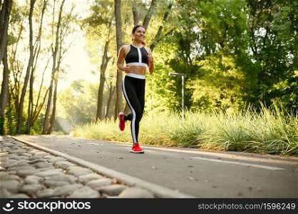 Morning training in park, woman running on walkway. Female runner goes in for sports at sunny day, healthy lifestyle, jogger on outdoors workout. Morning training in park, woman running on walkway