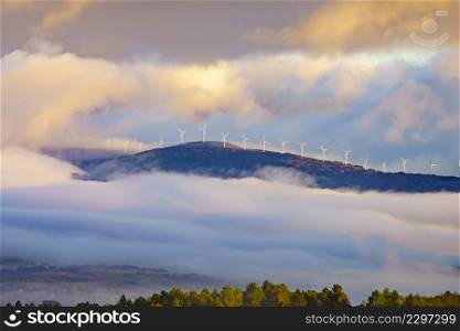 Morning view. Fog over valley and wind turbines farm on hill covered with clouds. Aguilar de Campoo in province of Palencia, Castile and Leon community, northern Spain.. Foggy valley and wind turbines in clouds