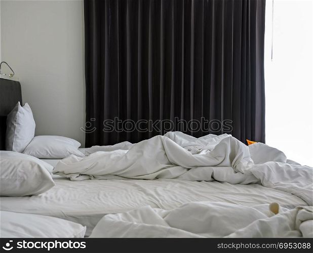 Morning view of an unmade rumpled bed in white bedroom interior with open curtain window