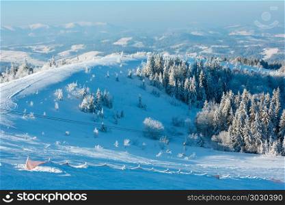 Morning winter calm mountain landscape with beautiful frosting trees in mountains shadows and ski slope (Carpathian Mountains, Ukraine). Winter mountain snowy landscape