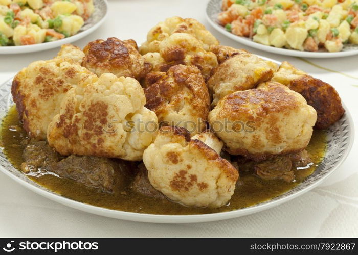 Moroccan traditional deep fried cauliflower with beef and sauce on a dish with potato salad as a side dish