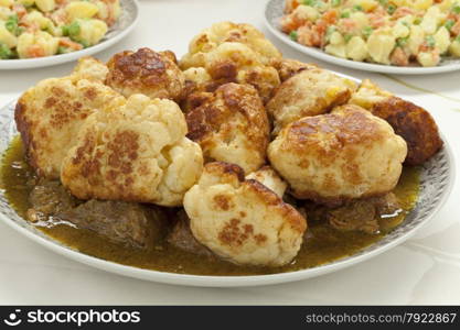 Moroccan traditional deep fried cauliflower with beef and sauce on a dish with potato salad as a side dish