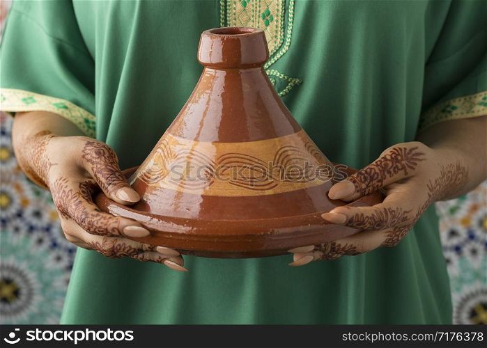 Moroccan woman with traditional henna painted hands holding a tagine