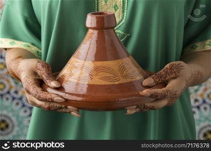Moroccan woman with traditional henna painted hands holding a tagine