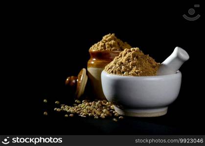 mortar and pestle with Coriander Powder and seeds on black background.