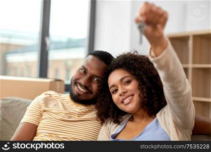 mortgage, eco living and real estate concept - happy african american couple with house key and boxes moving to new home and kissing. happy couple with house key moving to new home