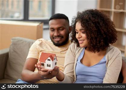 mortgage, eco living and real estate concept - happy african american couple with house model and boxes moving to new home. happy couple with house model moving to new home