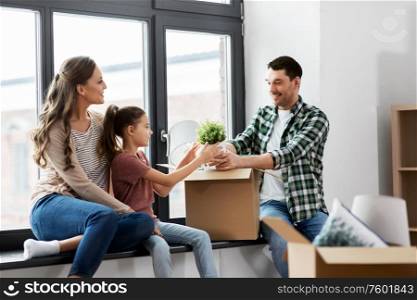 mortgage, family and real estate concept - happy mother, father and little daughter with stuff in boxes moving to new home. happy family with child moving to new home