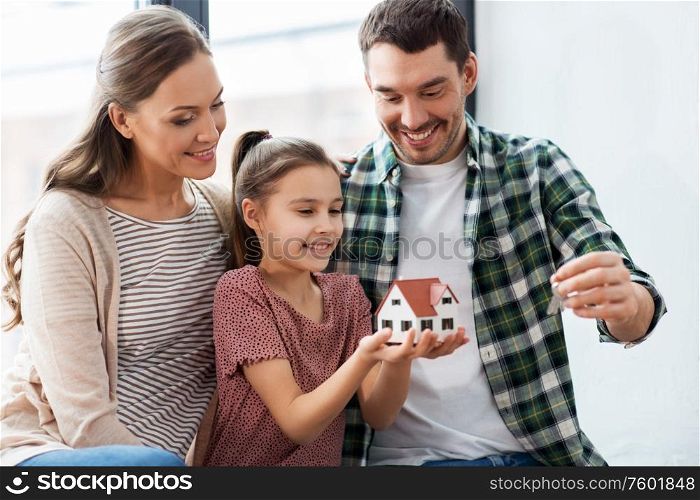 mortgage, family and real estate concept - happy mother, father and little daughter with house model and stuff in boxes moving to new home. happy family with house model moving to new home