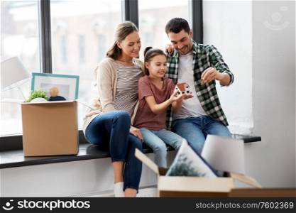 mortgage, family and real estate concept - happy mother, father and little daughter with house model and stuff in boxes moving to new home. happy family with house model moving to new home