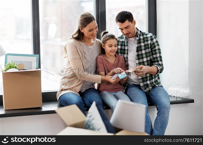 mortgage, family and real estate concept - happy mother, father and little daughter with color palette and stuff in boxes moving to new home. happy family with color palette moving to new home