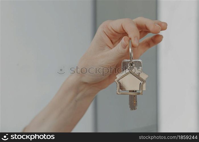 Mortgage loan investment. Female hand holding house shaped keychain, cropped shot of woman showing keys from new flat, buying real estate and moving at new home or renting apartment. Woman holding house shaped keychain, selective focuse on female hand with key from new home