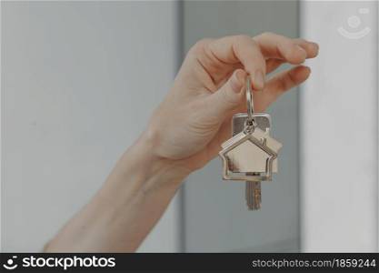 Mortgage loan investment. Female hand holding house shaped keychain, cropped shot of woman showing keys from new flat, buying real estate and moving at new home or renting apartment. Woman holding house shaped keychain, selective focuse on female hand with key from new home